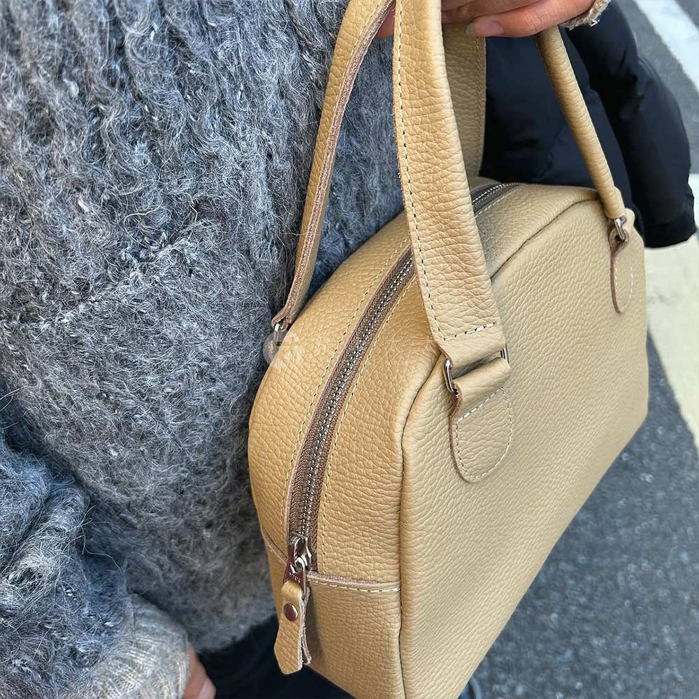 卡其色皮革迷你手提包，帶有拉鍊開合和皮革提把，與灰色毛衣搭配。