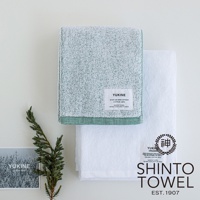 兩條 YUKINE 雪中漫步有機棉蓬厚迷你浴巾，一條為淺綠色，另一條為白色。兩條浴巾均為純棉材質，帶有品牌標籤，並配有綠色植物裝飾。