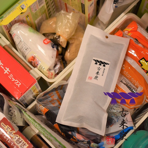 白色包裝袋內是細長的黑色調濕木炭，包裝上有印製日文「古來炭」字樣及品牌標誌，產品周圍有其他食品包裝。