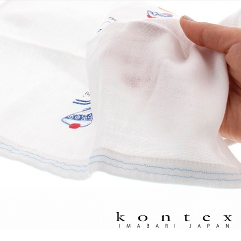 白色二層紗布巾，表面印有藍色與紅色的魚紋圖案，邊緣有藍色縫線。一隻手正在展示紗布巾的輕薄質地。