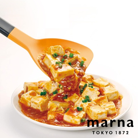 marna TOKYO 1872 品牌標誌旁，以橘色矽膠鍋鏟盛起一盤熱騰騰的麻婆豆腐，豆腐塊裹覆著濃郁醬汁，撒上翠綠蔥花，誘人美味。