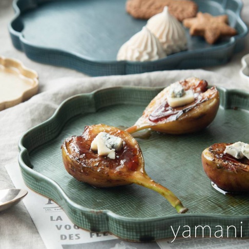 展示一個帶有波浪狀邊緣的綠色花型美濃燒主食盤，盤中盛有烤無花果，無花果上淋有醬汁並撒有藍紋起司。