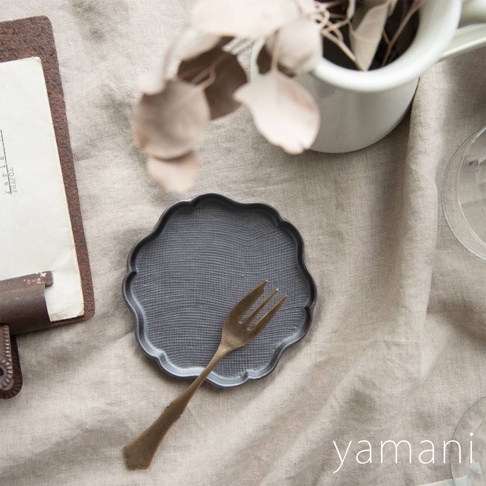 深灰色美濃燒花型小盤，盤面有細緻的織紋，搭配一支金屬色叉子。