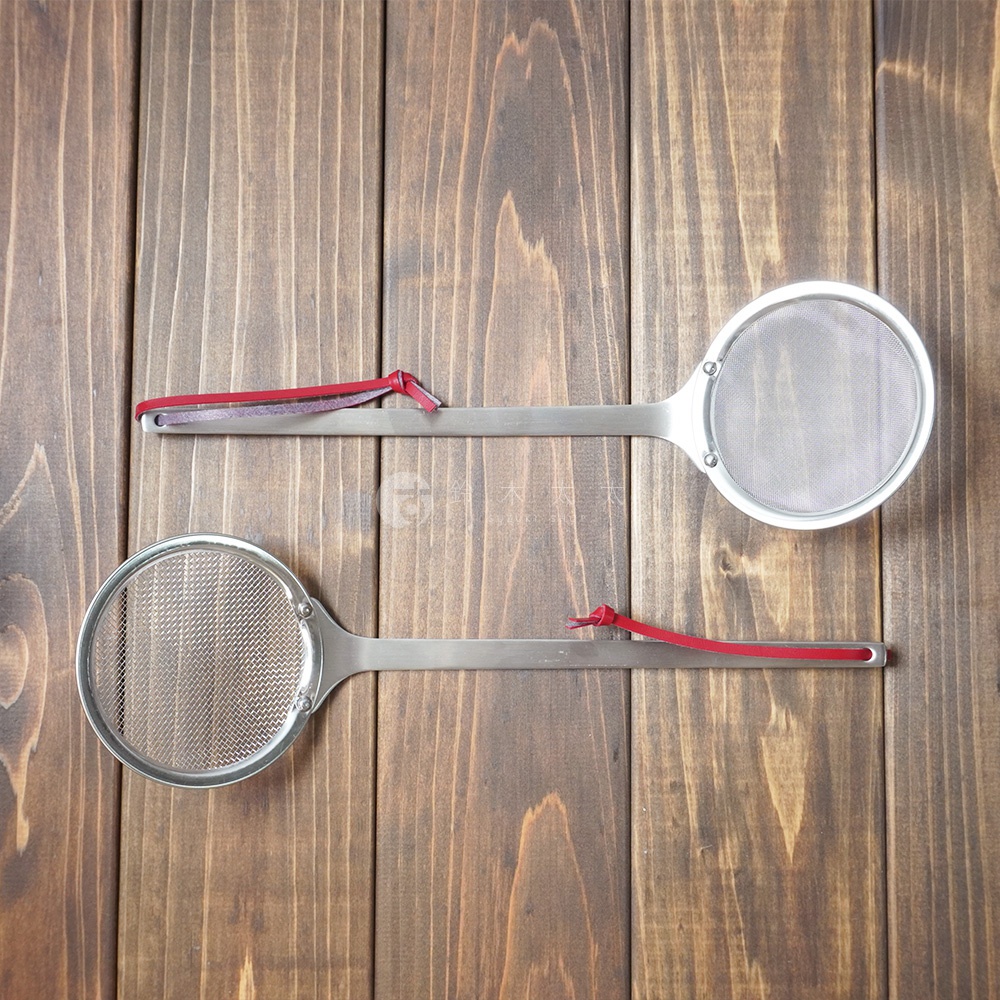 兩支不鏽鋼萬用撈油勺，一支給著紅色繫繩，另一支給著紅色繫繩，擺放在木紋背景上。