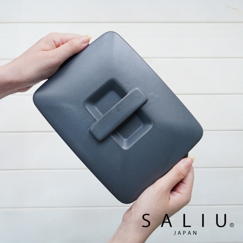 一隻手拿著深灰色、帶有中央提把的長方形陶製烤盤蓋，另一隻手扶著烤盤側邊。