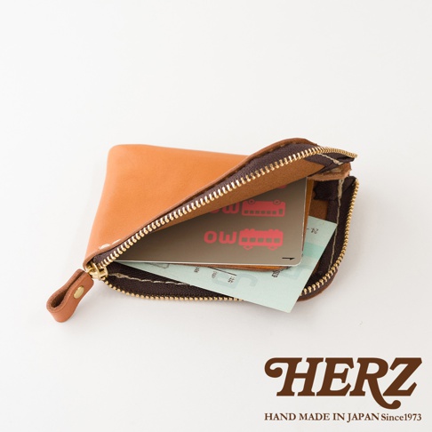 日本HERZ職人手作皮革零錢包，選用棕色皮革製成，拉鍊開口設計，內部裝有交通卡與票券，以俯視角度呈現其簡約小巧的質感。