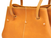 職人手作皮革可調式兩用大容量托特包 (Q-15)，採用溫暖的橘褐色真皮材質，包身有明顯的白色縫線，兩側各有一個圓形金屬扣飾，提把設計簡約。