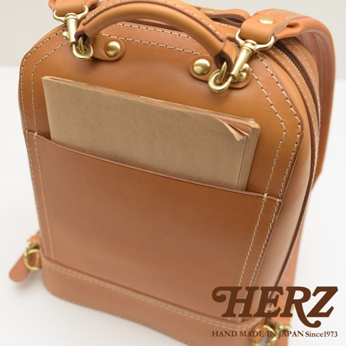 職人手作皮革立體商務後背包，採用溫潤的棕色牛皮材質，搭配簡約的設計與精緻車縫線，前方設有方便置物的 открытый 口袋，內嵌一本淺棕色筆記本。