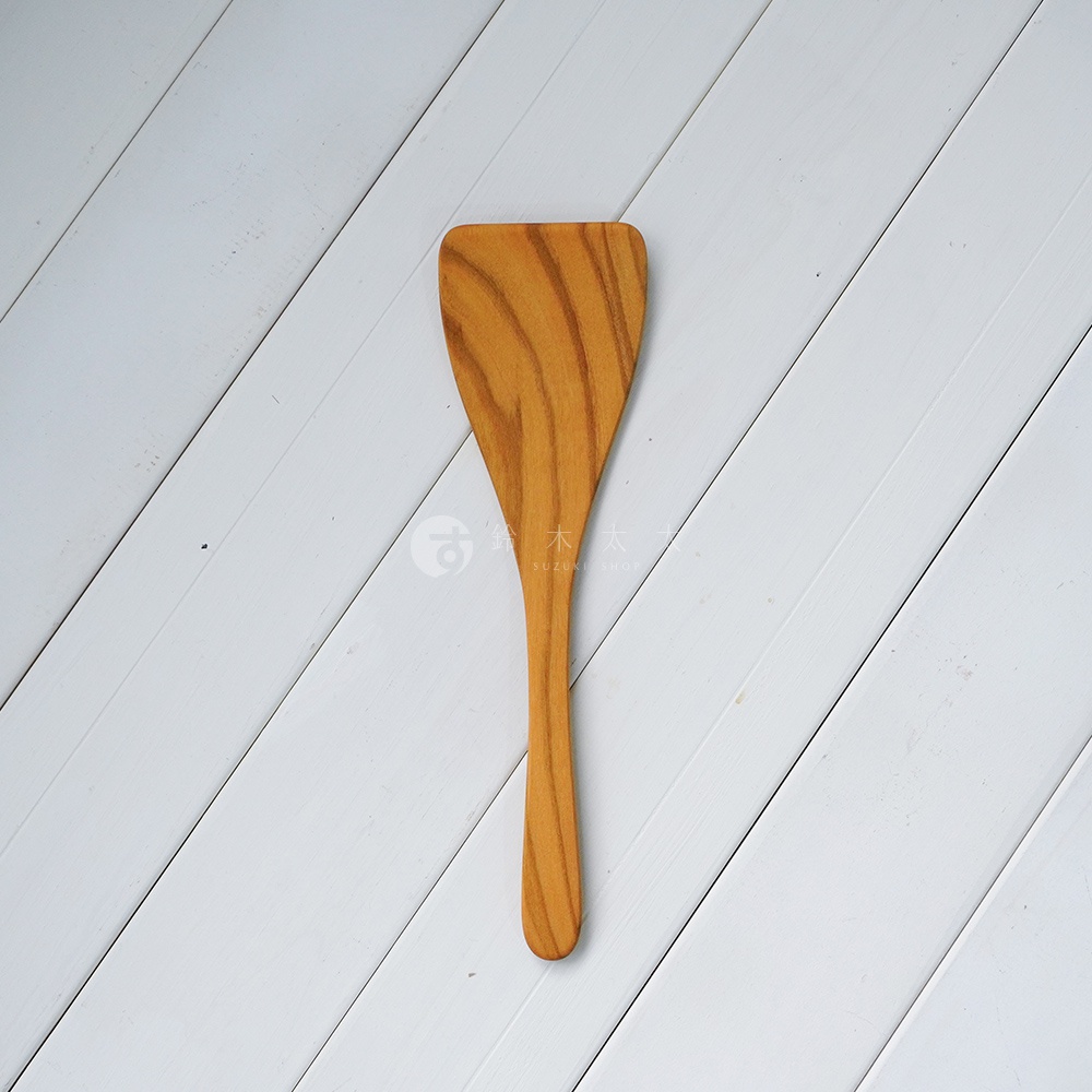 YAMASAKURA 山櫻木平口鍋鏟，木質呈現自然紋理與溫潤的淺棕色調，鍋鏟頭呈寬闊的扇形，手柄細長，整體為簡約的翻面用設計。