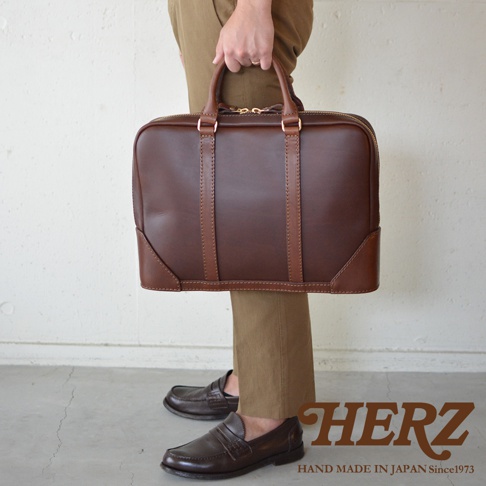 職人手作皮革Organ商務公事包 G-40，採用深棕色皮革，設有雙提把、金色拉鍊及雙色皮革拼接邊角，展現精緻工藝。