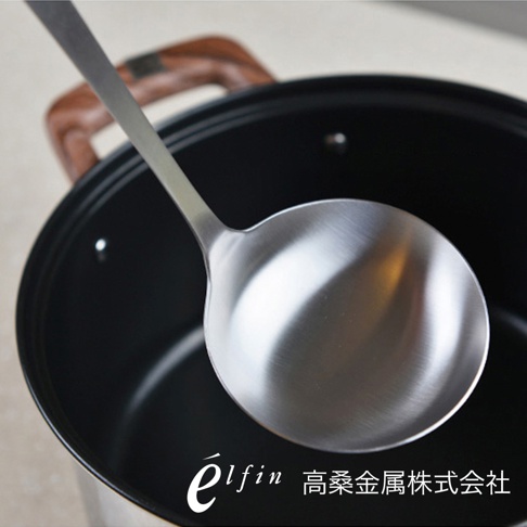 日製不鏽鋼湯杓，湯勺為銀色霧面金屬質感，手柄為深棕色木質，整體置於黑色鍋內，湯勺靠近鍋邊。