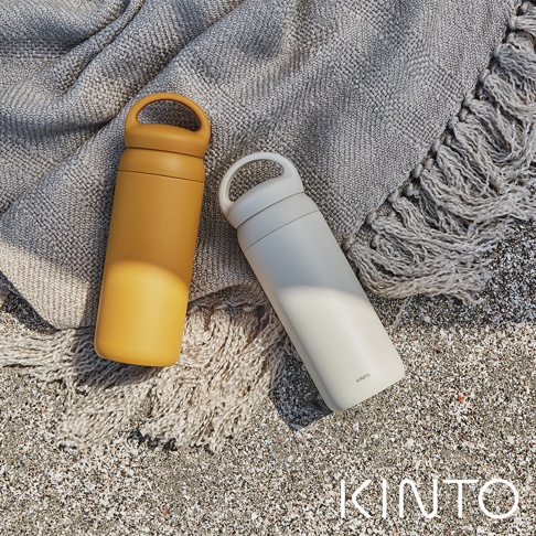 黃色和米白色DAY OFF提式輕巧保溫瓶，瓶身材質為不鏽鋼，帶有簡潔的提環設計，置於沙灘上的紋理毯子上。
