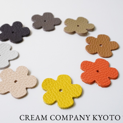 多款顏色（如深灰、淺棕、橘紅、亮黃、米白）的皮革花朵吊飾，皆為五瓣花造型，中央有圓孔，皮革表面帶有紋理。