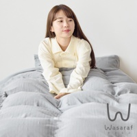 在灰色床鋪上，一位留著褐色長髮的年輕女子身穿米黃色長袖襯衫，露出微笑，視線看向右方。下方角落印有 W 字樣的 Logo 和 Wasaraf 文字。