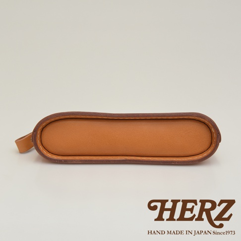 職人手作皮革三角弧形收納筆袋，採用光滑的棕褐色皮革製成，邊緣以深棕色皮革包邊並縫線，造型簡約，左側附有皮革提環。