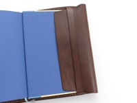 棕色皮革翻蓋記事本書套，內裡為藍色，展示書套部分結構與材質。