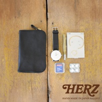 黑色皮革雙拉鍊收納袋，搭配一個白色錶盤黑錶帶的腕錶，一支金色筆，一個銀色鏡盒，內有金屬飾品，以及一張 SanDisk 512MB SD 記憶卡。