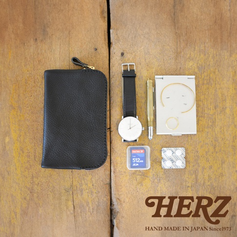 黑色皮革雙拉鍊收納袋，搭配一個白色錶盤黑錶帶的腕錶，一支金色筆，一個銀色鏡盒，內有金屬飾品，以及一張 SanDisk 512MB SD 記憶卡。