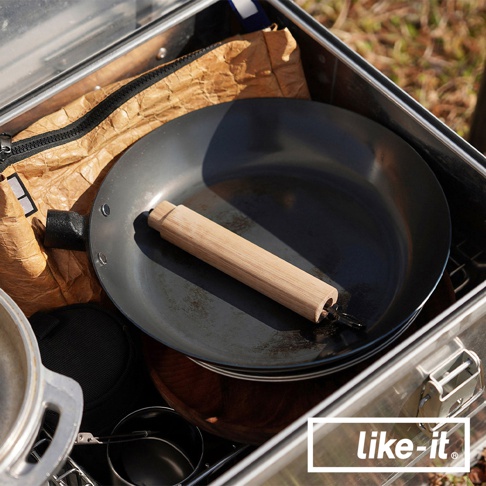 一個灰黑色的 26 公分直火專用萬能調理鐵鍋，配有木質手柄，放在金屬收納盒內，旁邊有紙袋和鍋具。