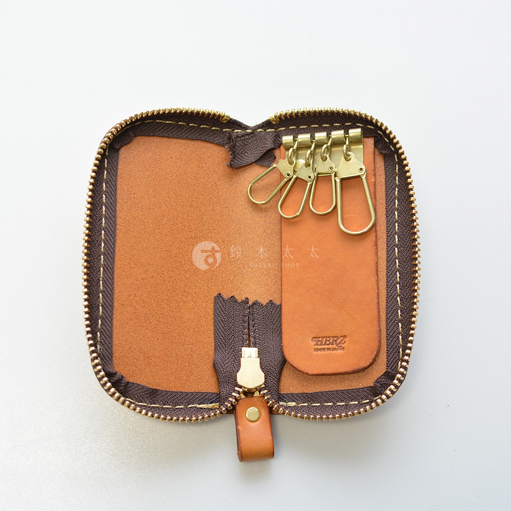 職人手作皮革鑰匙包，內有四個黃銅掛鉤，皮革內襯，拉鍊開闔，附有品牌標誌。