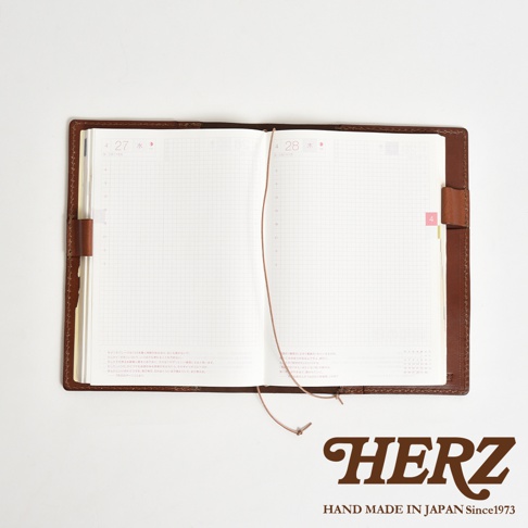 職人手作皮革手帳書套，打開的書頁內頁有方格，一條細繩連接兩頁，書套為棕色皮革，右下角印有HERZ LOGO。