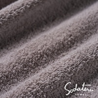 特寫畫面，展示一條淺灰色、蓬鬆柔軟的毛巾，其織物紋理清晰可見，並帶有品牌標誌 Sodateru TOWEL。