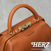 職人手作咖啡色皮革兩用口金手提包，帶有復古金色金屬鎖扣和圓弧形提把，皮革表面有細緻縫線與壓印品牌Logo。