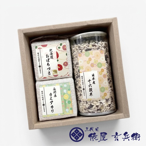 一個裝在簡約牛皮紙盒內的日本米禮盒，內含兩個方形真空包裝的白米與一個裝有日本產十六穀米的圓柱形透明罐，包裝袋與罐身標籤印有典雅的傳統日式花紋，右下角配有三代目俵屋玄兵衛的品牌標誌。
