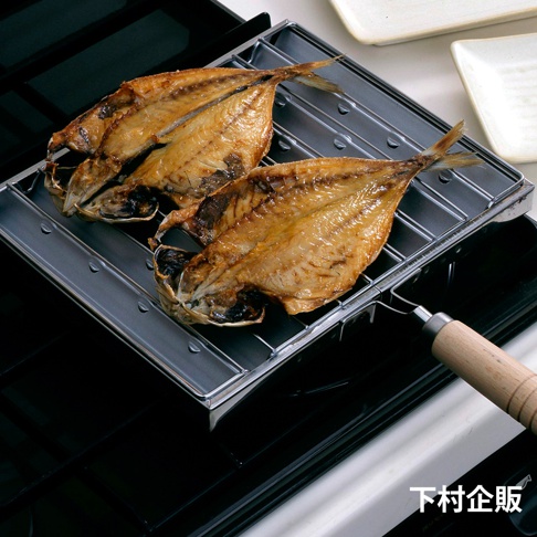 銀色金屬烤網上，兩條金黃色烤魚，魚皮油亮，魚肉熟透，烤盤下方為黑色瓦斯爐台，烤盤側面有木質手柄。