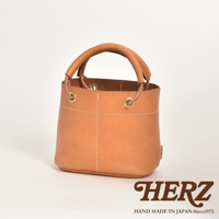 職人手作皮革加厚提把大開口午餐袋，採用柔軟的駝色皮革製成，設有加厚的圓形提把，透過縫線勾勒出立體感。袋口配有金屬孔和皮革抽繩，設計簡潔實用。