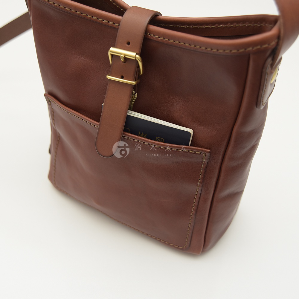 職人手作皮革輕便單肩側背包 CK-91，深棕色，採用光滑皮革材質，設有翻蓋扣帶、外插袋，袋內可見一本藍色護照。