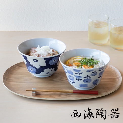 兩個波佐見燒藍花紋丼飯碗，其中一個裝有切片肉和洋蔥，另一個裝有麵條、蝦和檸檬片，擺放在木質托盤上，旁邊有兩杯飲品和一雙筷子。