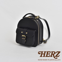 黑色皮革迷你後背包，圓潤造型，正面有翻蓋式口袋，配有黃銅釦環及皮帶。側邊有拉鍊開合，雙肩背帶可調。