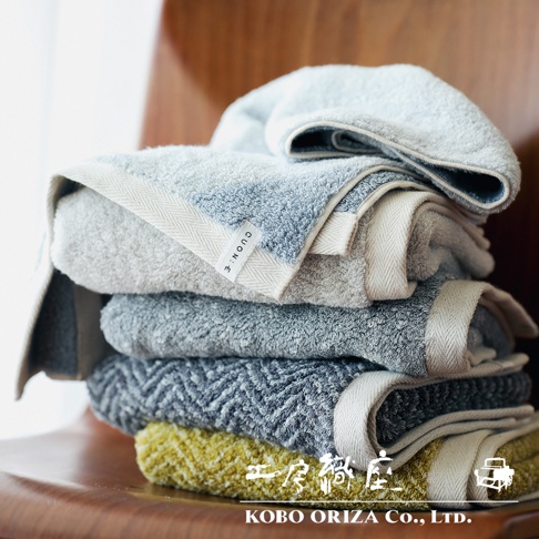 一疊棉麻混紡快乾毛巾，包含淺灰、淺藍、深灰和黃綠色。毛巾質地柔軟，部分有斜紋編織圖案，邊緣有白色滾邊。