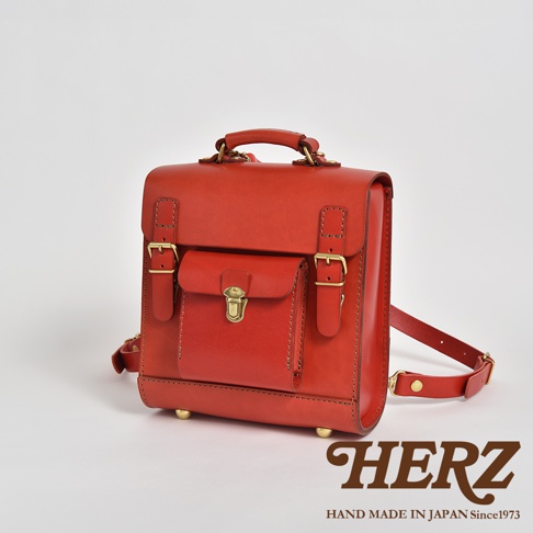 經典學院風迷你後背包，採用紅色皮革材質，配有金色金屬扣環和鎖扣，頂部有提把，側面有可調節的肩帶。