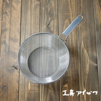 不鏽鋼濾網，帶有灰色矽膠握柄，網孔細密，置於木紋背景上。