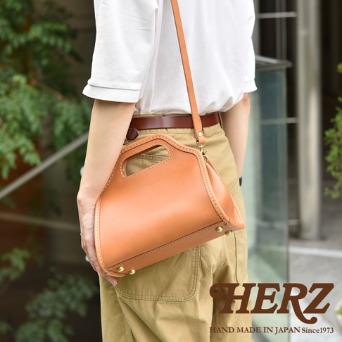 職人手作皮革單肩兩用拱型手袋，採用溫潤的棕褐色皮革，縫線清晰，側邊飾有金屬铆釘，可手提或斜揹。