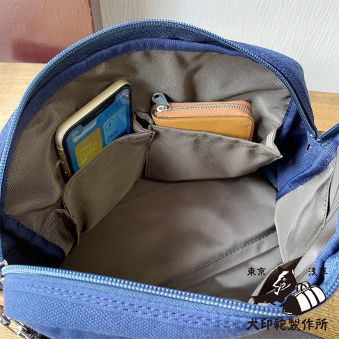 藍色石洗帆布旅行側背包內部，裝有手機和橘色零錢包，側邊有收納口袋。