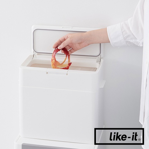 白色塑膠按壓式垃圾桶，掀開的蓋子內側有灰色密封條，一人手持蘋果皮準備丟入桶內。