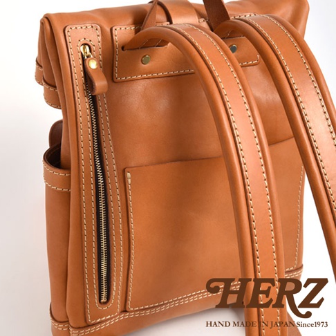 棕色皮革雙口袋折蓋後背包，有明顯的縫線和金色拉鍊，材質為皮革。