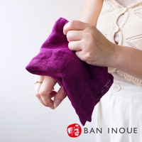 一塊深紫色、三層蚊帳棉織的迷你手拭巾，約37x37公分，織紋細緻，質地柔軟，由一雙手持握。