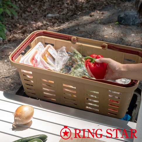 卡其色塑膠長型購物籃，裝有蔬菜、肉類和包裝食品。籃子有兩個紅色提把，側邊有長方形簍空設計。一只手正將一顆紅甜椒放入籃中。