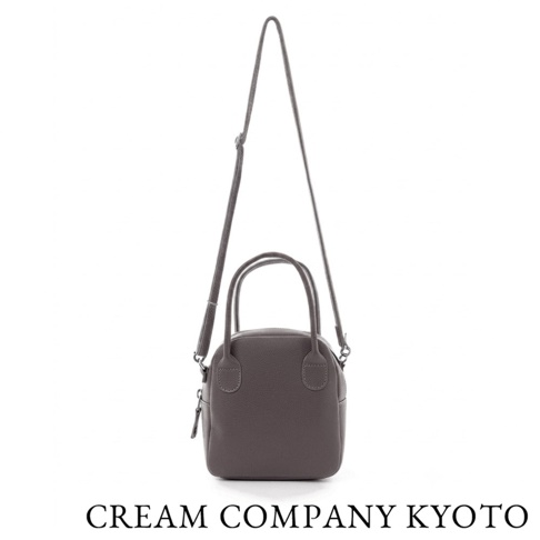 這款 CREAM COMPANY KYOTO 的京都職人手作貝殼包，採用質感灰色的輕量牛皮革製作，具備圓潤簡約的外型與實用的收納深度。包款配有可拆卸的細肩背帶與雙提把，支援肩背與手提雙重穿搭方式，底部印有品牌名稱。