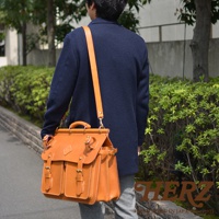 職人手作皮革旅行包 A-102，採用天然皮革製成，呈現溫潤的焦糖棕色。包款設計經典，配有頂部提把、可拆卸肩帶、多個金屬扣環以及前後雙層口袋，線條俐落，質感紮實。