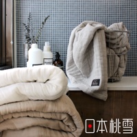 兩床八層紗透氣被，一床為米白色，另一床為淺褐色，皆為蓬鬆柔軟的材質。左側背景有白色瓶裝清潔用品及棕色瓶裝香皂，右側的淺灰色八層紗被裝在金屬籃中。