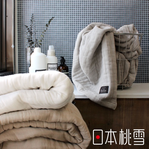 兩床八層紗透氣被，一床為米白色，另一床為淺褐色，皆為蓬鬆柔軟的材質。左側背景有白色瓶裝清潔用品及棕色瓶裝香皂，右側的淺灰色八層紗被裝在金屬籃中。