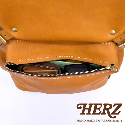 職人手作皮革多口袋後背包 R-135，展示了黃褐色皮革材質，包身設有拉鍊式前袋，袋內可見錢包與小型電子產品。