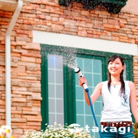 手持白色及藍色噴嘴的灑水器，正向外噴灑水花。背景為磚牆和綠色窗戶。