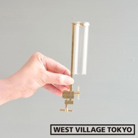 一只手持著黃銅可夾式玻璃花器，花器由黃銅支架和透明直筒形玻璃瓶組成，玻璃瓶帶有垂直紋理。