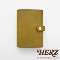 職人手作皮革手帳/記事本書套，採用黃褐色皮革製成，表面有一條皮革束帶及金色按扣，邊緣以細緻車縫線裝飾。